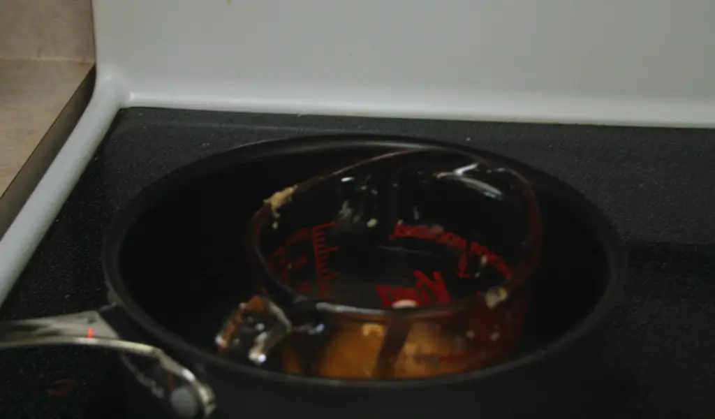 Beeswax melting in a measuring cup in boiling water.