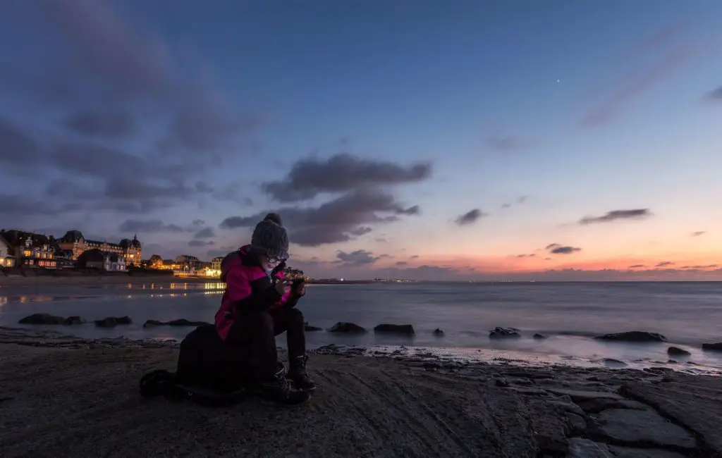a woman sits on a beach looking at her phone, looking at poetry or writing poems on instagram