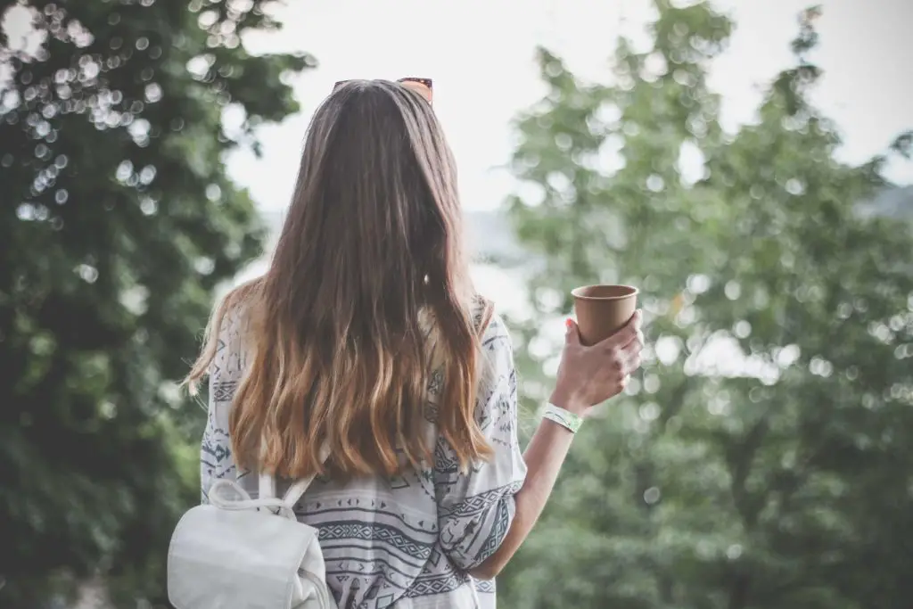 a woman holding a coffee living siply and embracing the Slow Life trend, standing amongst the trees.