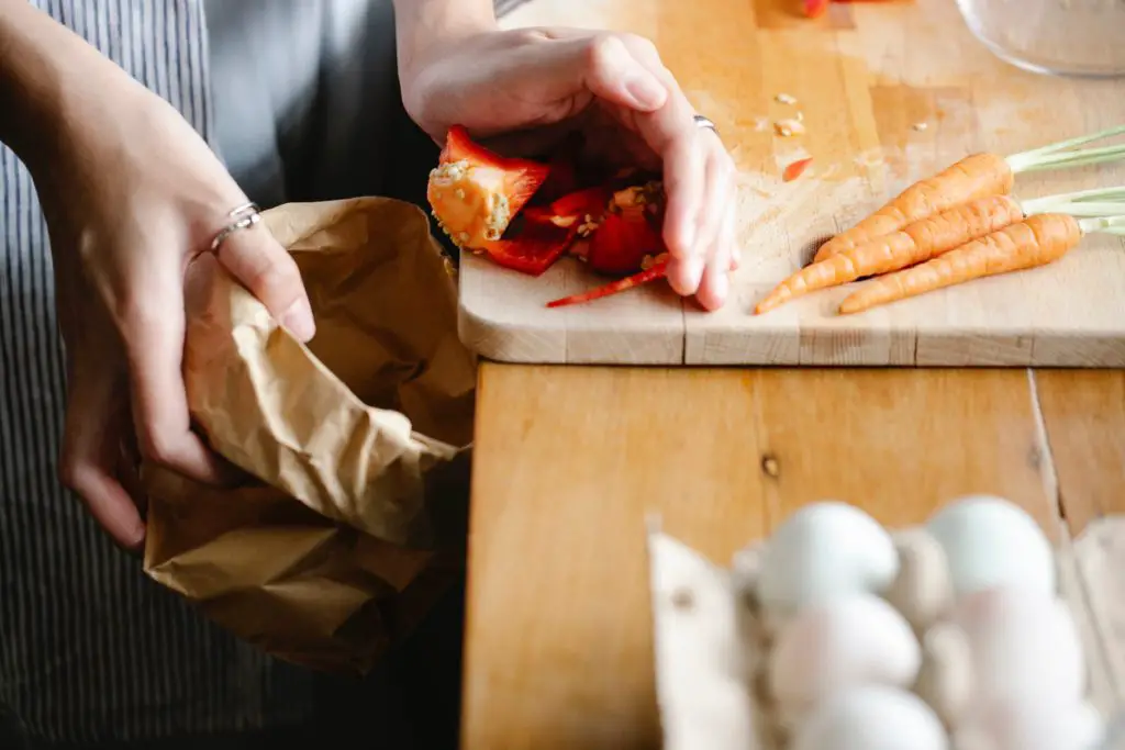 a woman is putting her organic waste into a paper bag, to put into her compost.