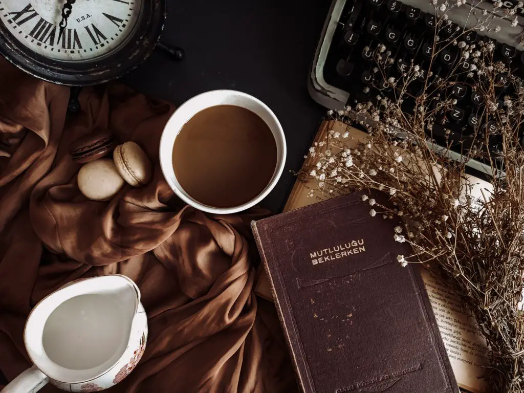 A dark academia aesthetic photo, including dried flowers, a notebook, and a coffee.