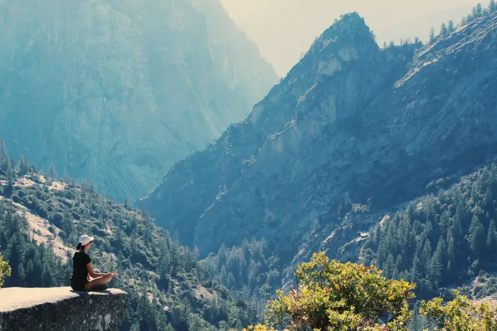 A woman sits on the edge of a cliff, basking in the mountains. This is the practice of forest bathing.