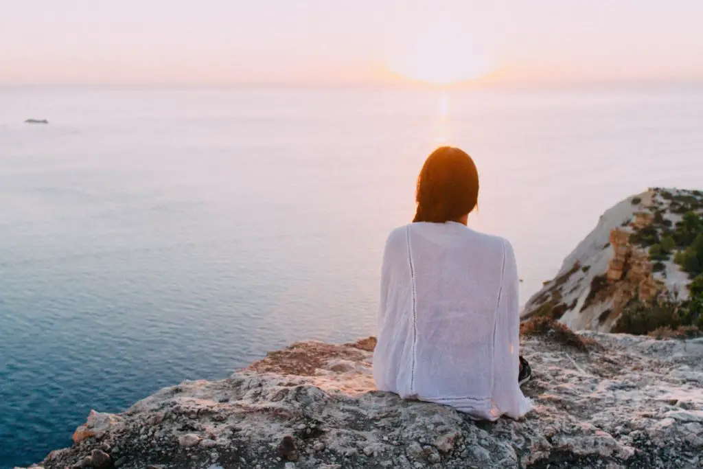 a woman sits on the egde of a cliff looking at the ocean. This picture represents the end of summer, and reflects on the season.