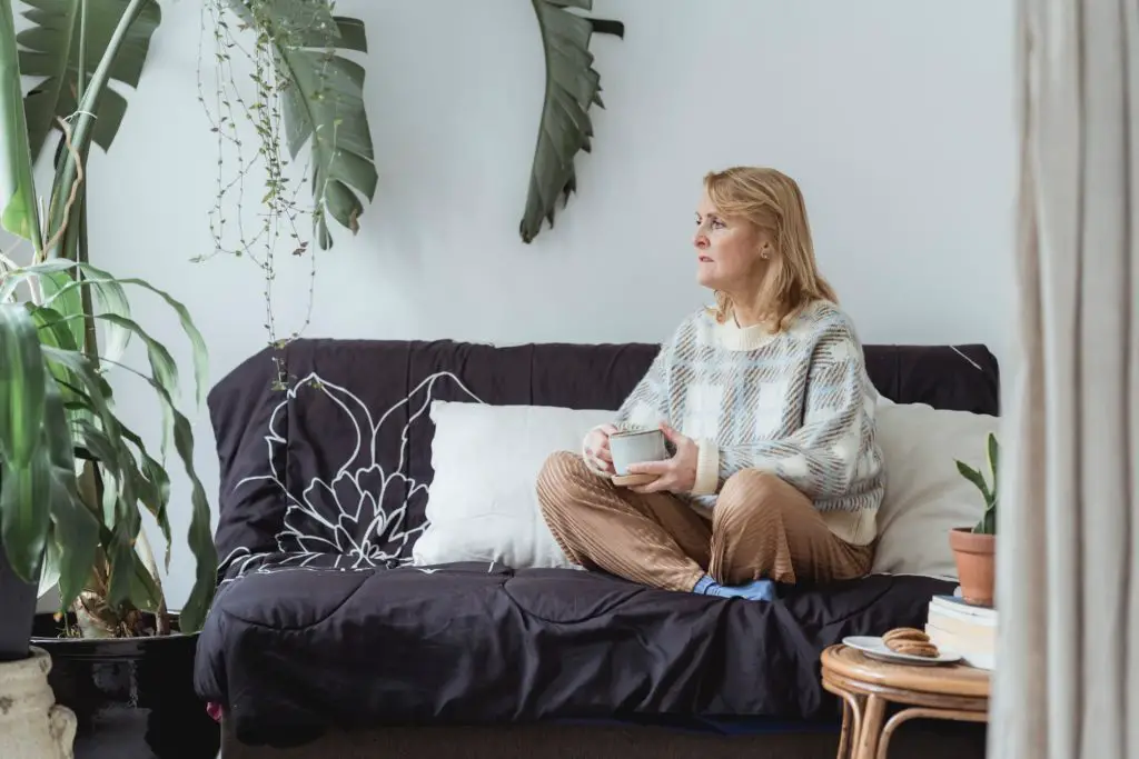 A woman looking cozy on her couch sitting alone comfortably in her living room, embracing the joy of missing out.