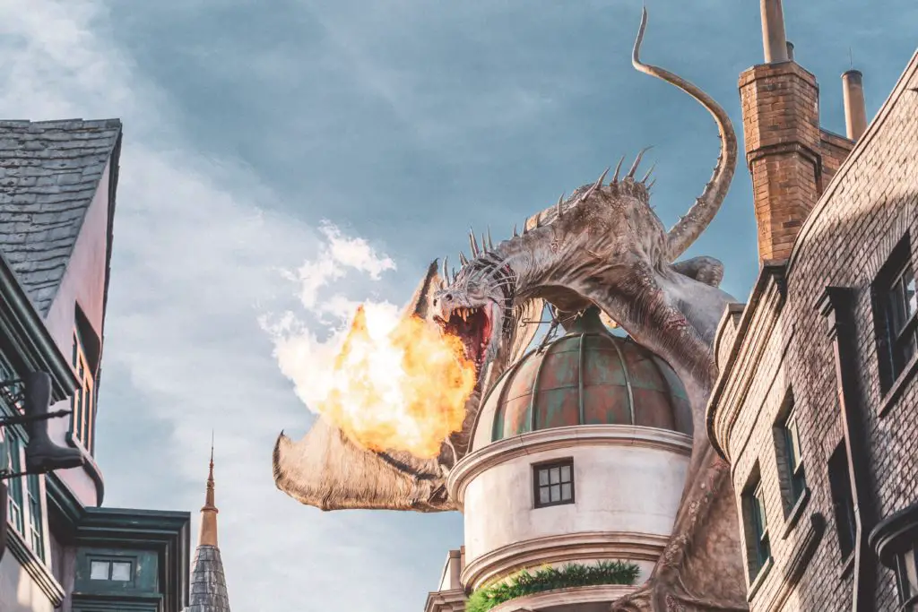 A dragon sits on top a castle roof breathing fire in this high fantasy image.