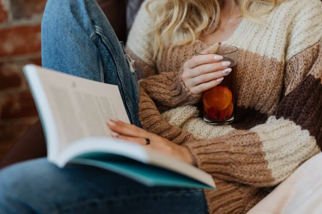 this photo is an example of the essence of hygge, you can see a woman wearing a cozy sweater reading a book.